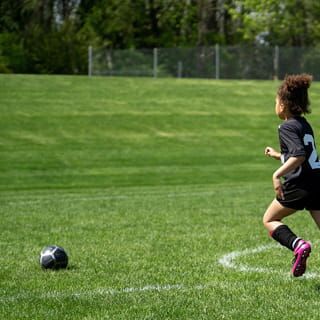 Fußballspieler läuft auf gepflegtem Rasen zum Ball auf einer Sportanlage mit professioneller Bewässerung