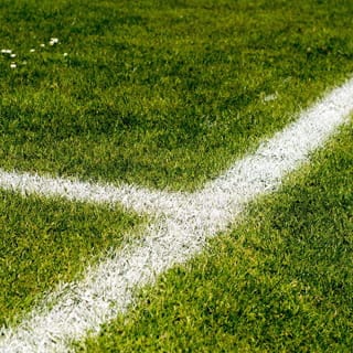 Eine Bewässerungsanlage für einen Sportplatz: Detailaufnahme von Rasen mit weißen Spielfeldlinien als Hinweis auf gepflegte Sportfläche und professionelle Sportplatzbewässerung