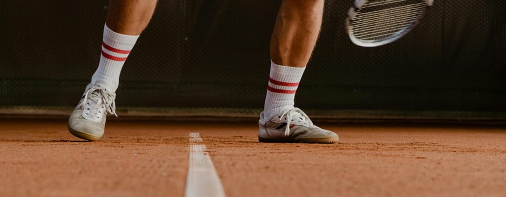 Dynamische Nahaufnahme eines Tennisspielers beim Slide auf Ziegelmehl zur Verdeutlichung der notwendigen Bodenhaftung durch professionelle Bewässerung