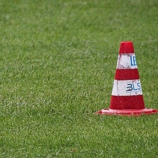 Trainingskegel auf einem bespielbaren Rasenplatz im laufenden Sportbetrieb