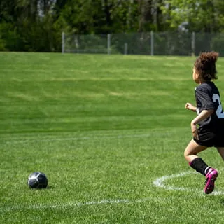Fußballspieler läuft auf gepflegtem Rasen zum Ball auf einer Sportanlage mit professioneller Bewässerung