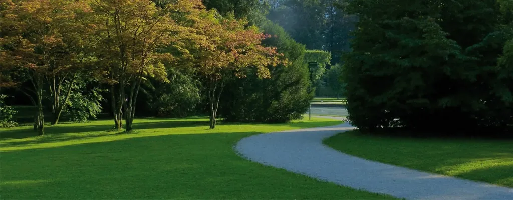 Eine weitläufige, gepflegte Parkanlage mit grünem Rasen, Bäumen und einem geschwungenen Spazierweg vor einer Bergkulisse – ein Beispiel für durch Bewässerungssysteme erhaltene öffentliche Grünflächen