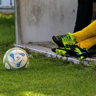 Fußball am Spielfeldrand neben Spielerbeinen auf Rasen als Motiv für Sportplatzbewässerung und gleichmäßige Bewässerung von Sportplätzen