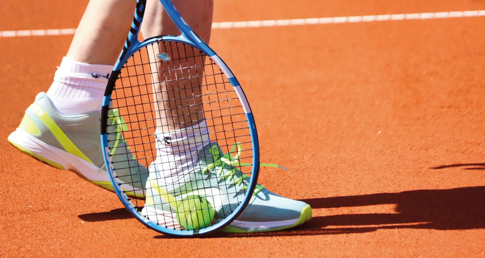 Beregnungsanlagen für Tennisplätze: Nahaufnahme eines Tennisspielers auf einem Sandplatz zur Veranschaulichung der idealen Bodenfeuchte und Scherfestigkeit durch professionelle Bewässerungstechnik