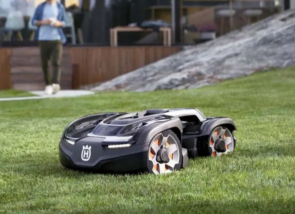 Professionelle Mähroboter : Ein leistungsstarker Husqvarna Automower Mähroboter im Einsatz auf einer gepflegten Rasenfläche mit Steigung zur Demonstration von Geländegängigkeit und präzisem Schnitt