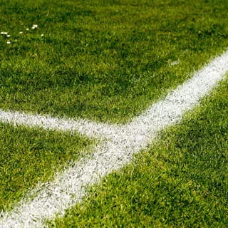 Eine Bewässerungsanlage für einen Sportplatz: Detailaufnahme von Rasen mit weißen Spielfeldlinien als Hinweis auf gepflegte Sportfläche und professionelle Sportplatzbewässerung