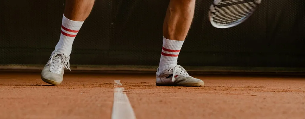 Dynamische Nahaufnahme eines Tennisspielers beim Slide auf Ziegelmehl zur Verdeutlichung der notwendigen Bodenhaftung durch professionelle Bewässerung